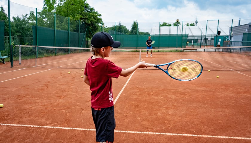 Powiększ obraz: Na zdjęciu chłopiec grający w tenisa ziemnego z trenerem na jednym z kortów WCT Spartan we Wrocławiu