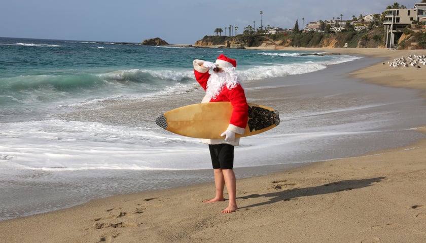 Powiększ obraz: Na zdjęciu święty Mikołaj na plaży z deską surfingową