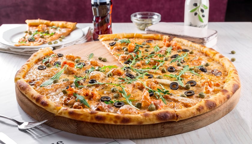 Powiększ obraz: Na zdjęciu pizza z czarnymi oliwkami.