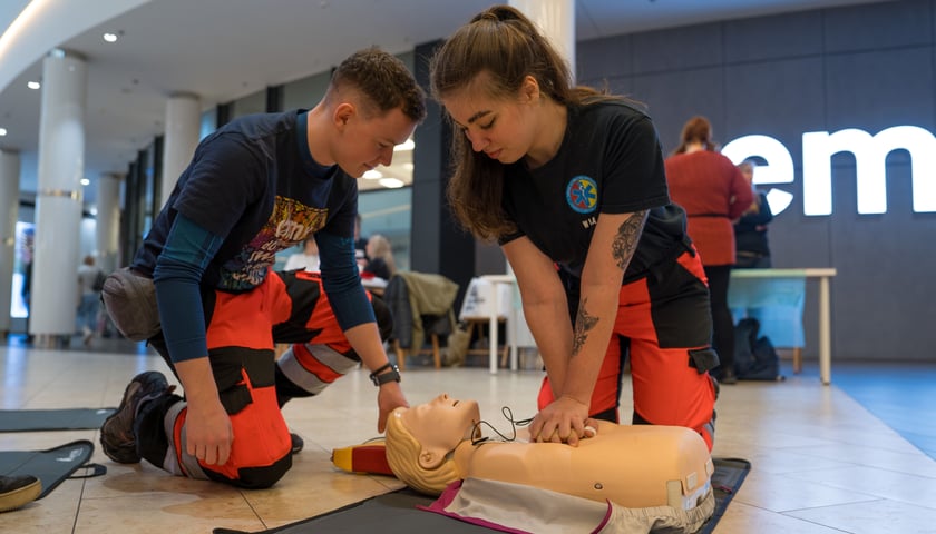 Powiększ obraz: Dwóch ratowników medycznych (kobieta i mężczyzna) pokazuje jak udzielić pierwszej pomocy na fantomie