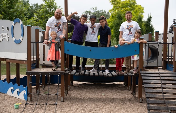 Powiększ obraz: Trzech ojców w białych koszulkach z pięciorgiem dzieci na placu zabaw na Wyspie Bielarskiej