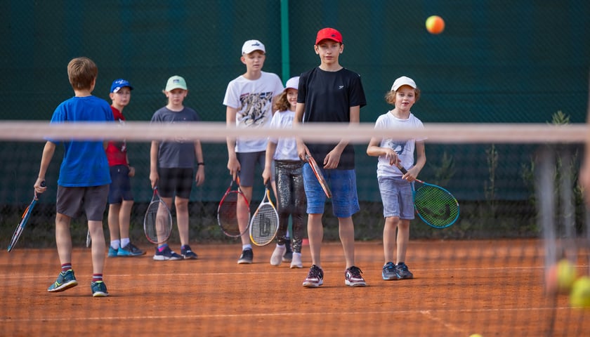 Powiększ obraz: Dzieci po jednej stronie siatki z rakietami odbijają piłki tenisowe