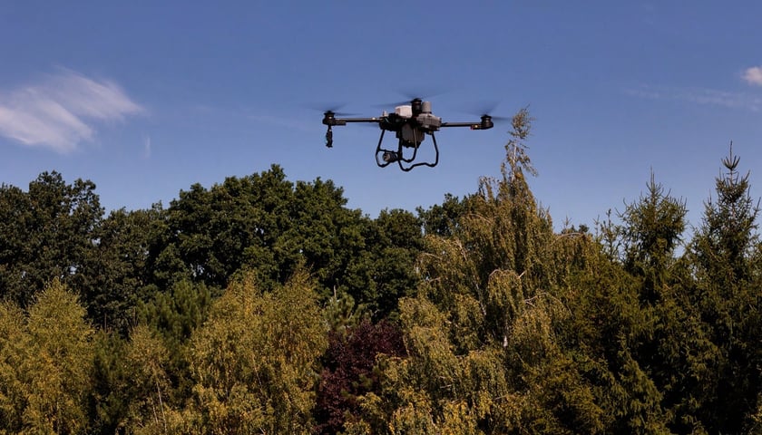 Powiększ obraz: Dron z opryskiem przeciwkomarowym, działającym wyłącznie na larwy, nad zbiornikiem wodnym na tle gęstego drzewostanu