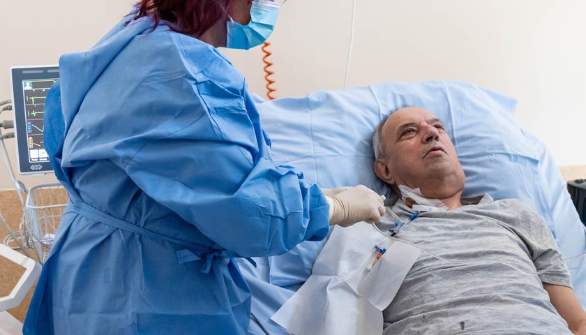 Pacjent leżący na szpitalnym łózko i lekarka podająca wlew. Jan Kowalski otrzymuje  zmodyfikowane limfocyty w ramach terapii CAR-T w Klinice Hematologii UMW.