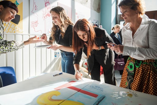 Powiększ obraz: Cztery kobiety pochylone nad stołem, podpisujące się przy literze T od napisu MOST