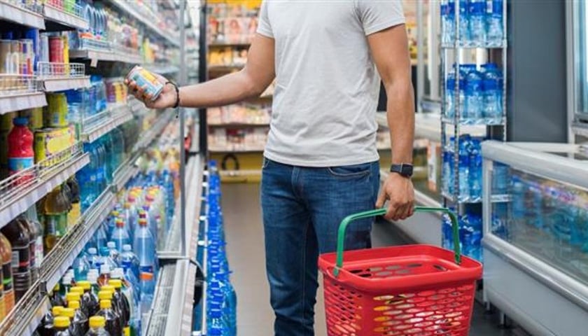 Powiększ obraz: Sylwetka mężczyzny z czerwonym zakupowym koszykiem w ręce, w drugiej trzyma napój w puszce