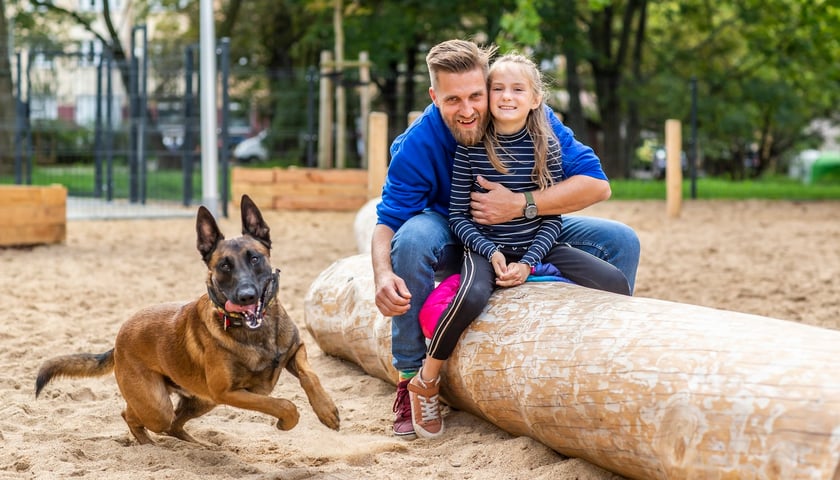 Powiększ obraz: Ojciec z córką i psem rasy owczarek niemiecki na placu zabaw dla czworonogów Psia Hubka