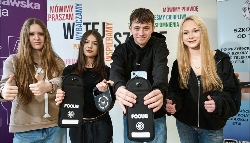 Powiększ obraz: Czworo uczniów ze Szkoły Podstawowej 50 przy ul. Czeskiej: Aleksandra, Julia, Mikołaj i Marysia pozują do zdjęcia; Julia i Mikołaj pokazują etui blokujące sygnał smartfonów