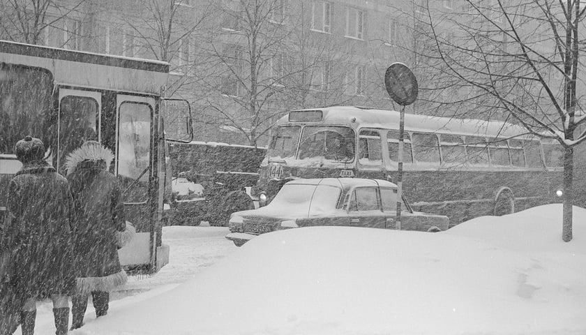 Powiększ obraz: Pasażerowie próbują wsiąść do autobusu na zasypanym śniegiem przystanku