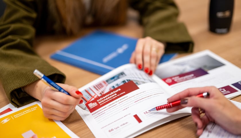Powiększ obraz: Dwie osoby czytają folder z ofertą  infrastruktury przemysłowej w WPT