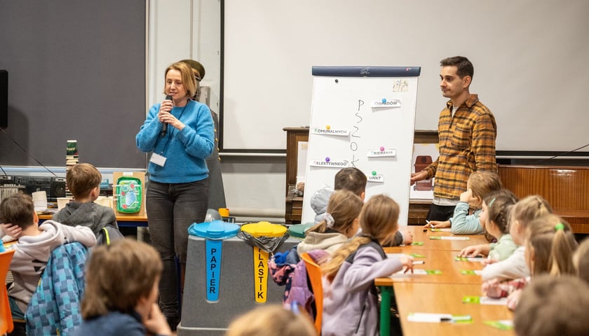 Powiększ obraz: Zajęcia w klasie - dwóch prowadzących (kobieta i mężczyzna) przed grupą dzieci