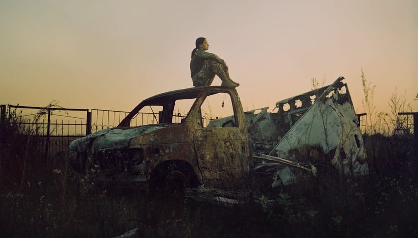 Kadr z filmu "Mariinka". Na zdjęciu kobieta w wojskowym mundurze siedzi na wraku spalonego samochodu.