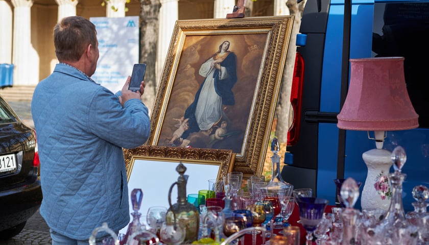 Giełda staroci koło Hali Stulecia. Na zdjęciu widać mężczyznę, który robi zdjęcie telefonem komórkowym. Mężczyzna fotografuje piękny obraz