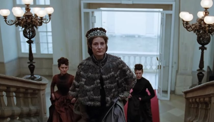 Kadr z filmu „W gorsecie” o cesarzowej Sissi. Zdjęcie przedstawia główną bohaterkę w pałacu oraz dwie inne kobiety