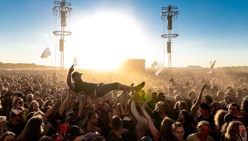 Publiczność Pol'and'Rock Festivalu niesie na rękach młodego mężczyznę w czapce z daszkiem i okularach