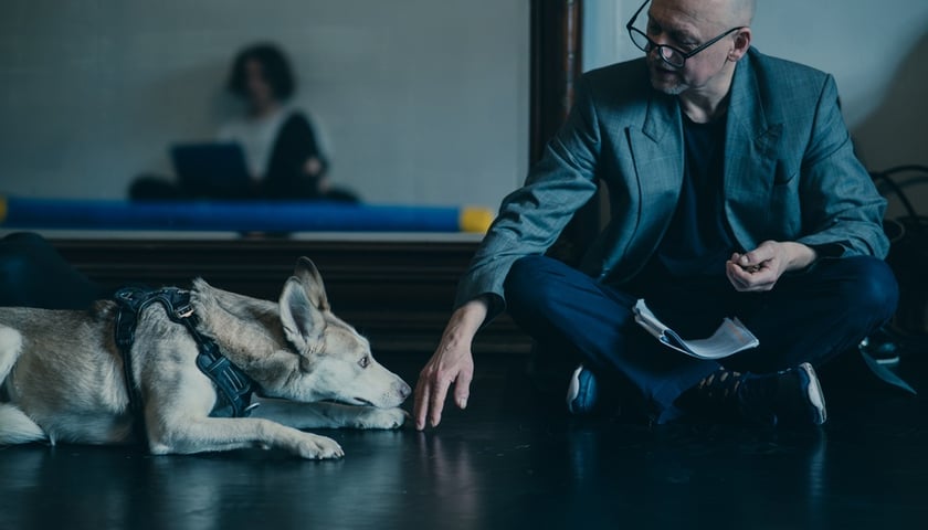 Siedzący po turecku mężczyzna w okularach i leżący przy nim pies