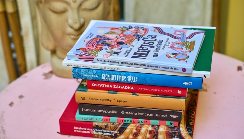 Na zdjęciu polecane książki ułożone w stosik na niebieskim stoliku