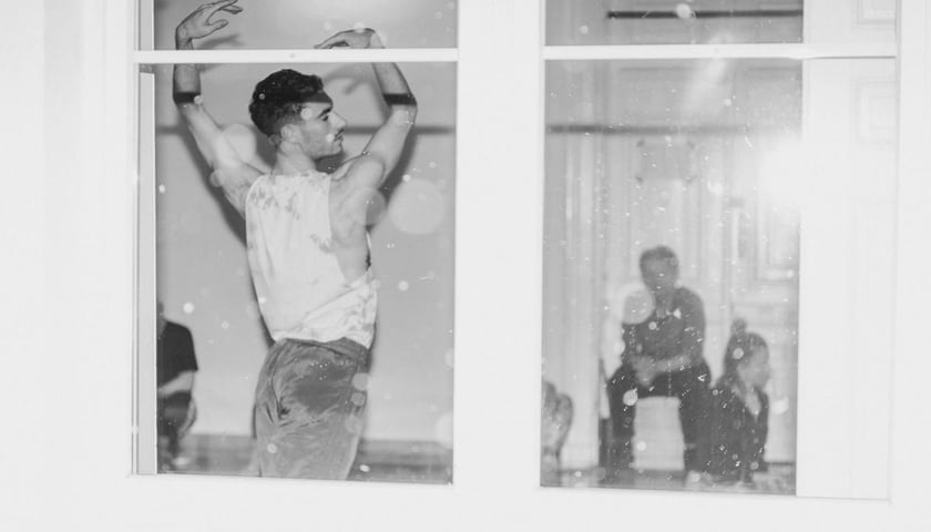 Mężczyzna w koszulce bez rękawów widziany przez okno, zdjęcie z próby do "Złych Baśni".