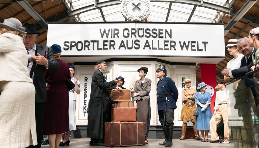 Jedna ze scen filmu "Breslau" została nakręcona na dworcu Wrocław Główny. Na zdjęciu pasażerowie i policjant. Nad nimi napis po niemiecku - Witamy sportowców z całego świata.