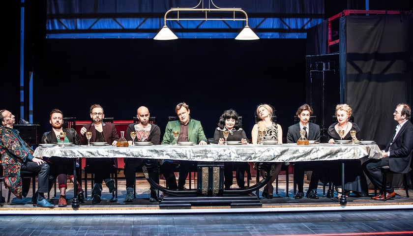 Na zdjęciu scena ze spektaklu Krystiana Lupy, aktorzy siedzą przy stole