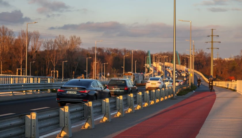 Powiększ obraz: Aleja Wielkiej Wyspy w blasku zachodzącego słońca. Droga rowerowa i oddzielona od niej ulica z samochodami