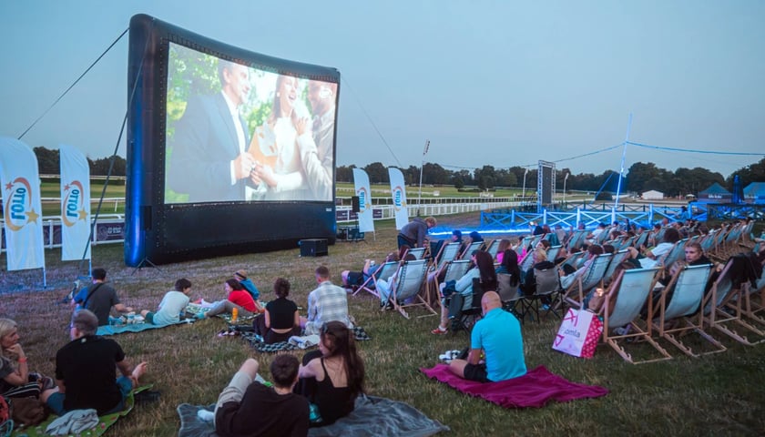Kino plenerowe na Partynicach. Widzowie oglądają film na ekranie, który stoi tuż przy torze wyścigowym.