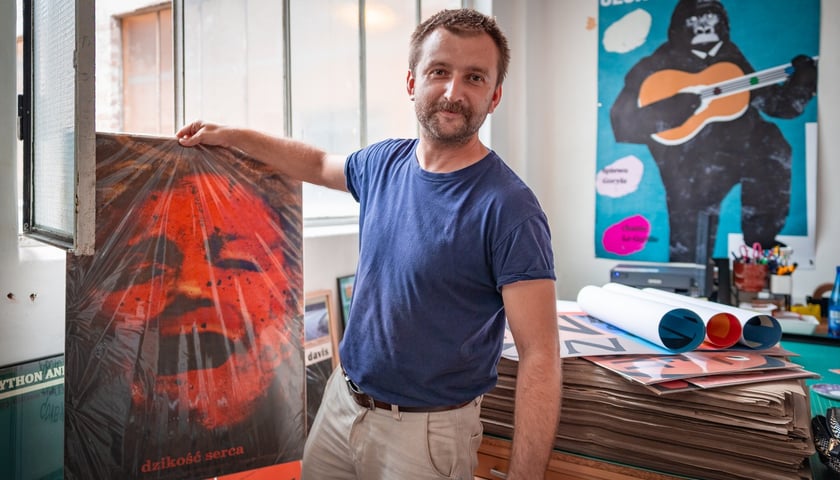 Na zdjęciu Jakub Zasada w swoim sklepie-pracowni z plakatem do filmu „Dzikość serca”, w tle jego plakat ukochany z Georges'em Brassensem 