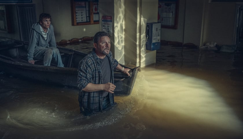 Bohaterowie serialu „Wielka woda” w szpitalu na Traugutta, aktor Ireneusz Czop stoi w wodzie po pas, aktor Damian Krajczyk siedzi w łodzi 