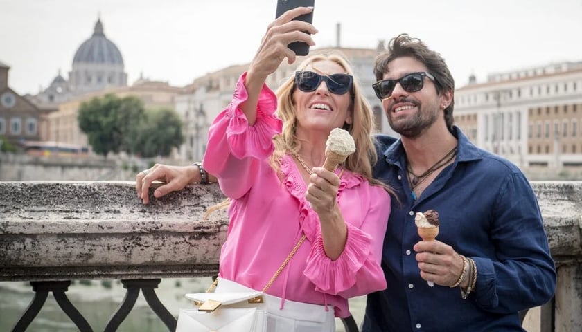 Aktorka i aktor grający główne role w filmie „Mafia Mamma” jedzą lody i robią sobie zdjęcie w Rzymie za pomocą kijka do selfie 