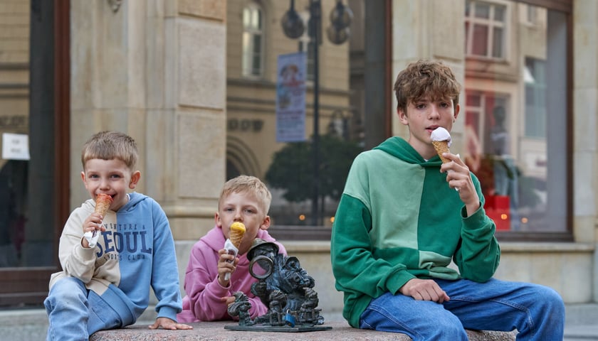 Trzech chłopców jedzących lody i siedzących przy krasnalce detektywie przed wrocławskim hotelem Monopol