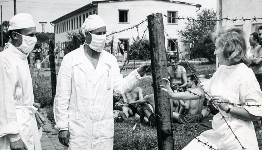 Izolatorium na Psim Polu podczas epidemii czarnej ospy. Na pierwszym planie dwóch mężczyzn w białych uniformach i maseczkach, obok uśmiechnięta kobieta w białym fartuchu. Zdjęcie Mieczysława Dołęgi ze zbiorów Muzeum Miejskiego Wrocławia. 