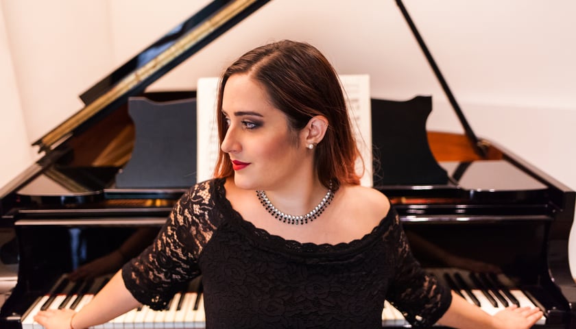 Leonora Armellini odwrócona profilem opiera się o klawiaturę fortepianu