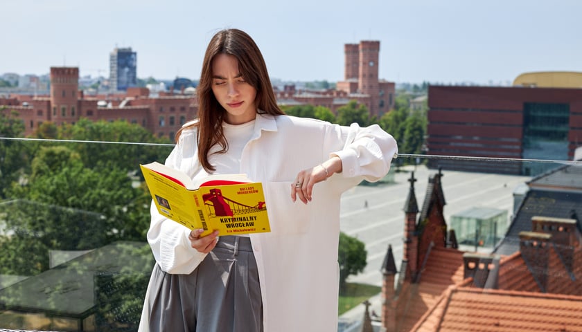 Młoda dziewczyna z długimi włosami czyta książkę, a w tle wieże sądu przy Podwalu we Wrocławiu