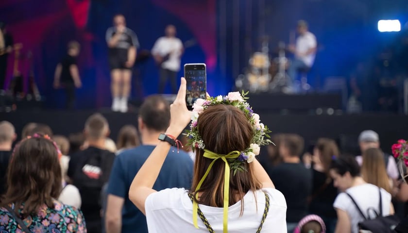 Kobieta w wianku robi smartfonem zdjęcie artystom występującym na scenie, koncert Letnie Brzmienia 2023 