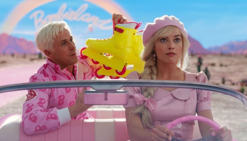 Kadr z filmu „Barbie”: Margot Robbie jako Barbie i Ryan Gosling jako Ken jadą samochodem z odkrytym dachem. Aktor siedzi z tyłu i trzyma żółte rolki