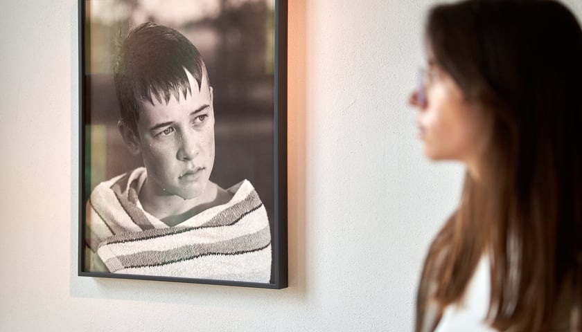 Kobieta oglądająca wiszące na ścianie Galerii BWA Wrocław Główny zdjęcie chłopca. Fotografia ilustracyjna