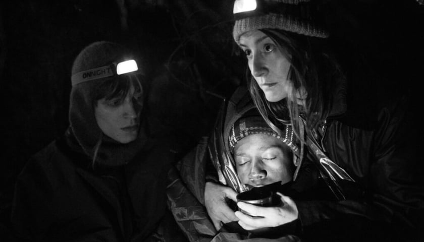 Kadr z filmu "Zielona granica". Julia (Maja Ostaszewska) pomaga nocą w lesie uchodźcom. Jednemu podtrzymuje głowę. Z lewej aktywista