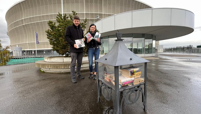 Renata Cierniak, kierowniczka filii nr 7 MBP (na zdjęciu po prawej) i Maciej Kozieł z MBP stoją przed stadionem, w rękach trzymają książki 