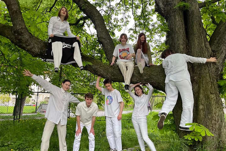 Chórzyści Angelusa w białych ubraniach pod drzewem i siedzący na drzewie