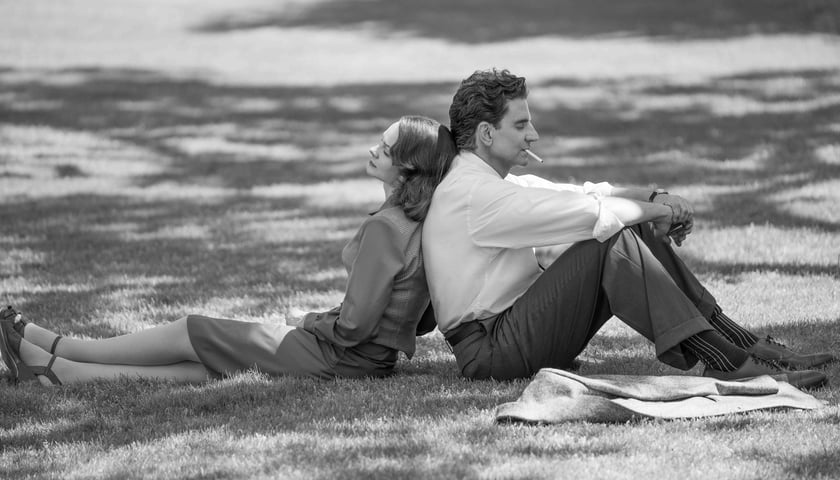 Mężczyzna i kobieta siedzą na trawie plecami do siebie, kadr z filmu „Maestro” na Netflixie