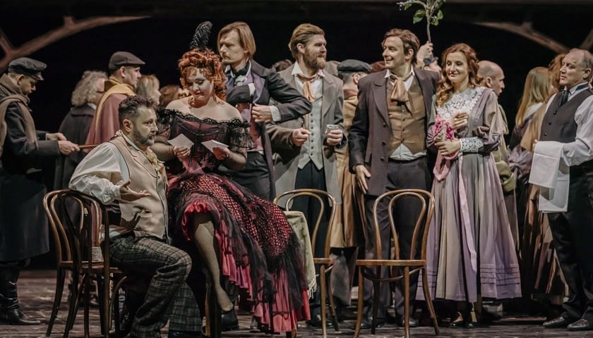 Scena zbiorowa z opery – w spelunce tłum artystów, kobieta siedzi mężczyźnie na kolanach, tuż obok stoi druga para