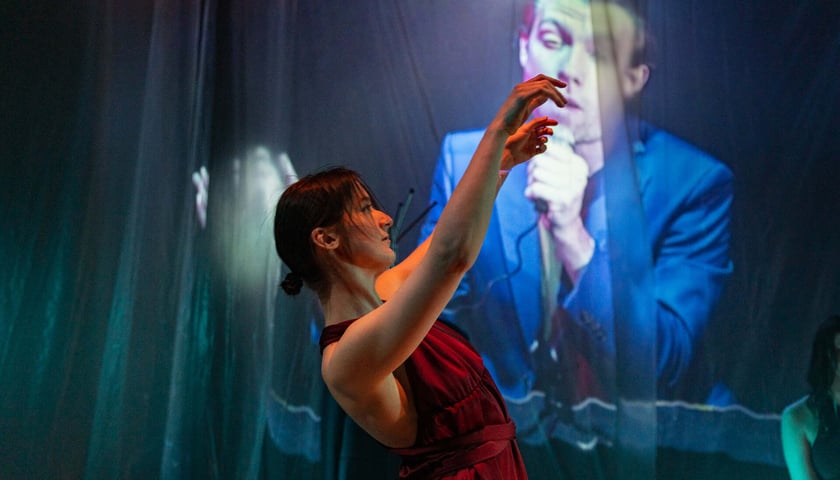 Spektakl Teatru na Faktach w Instytucie Grotowskiego. Na zdjęciu aktorka w bordowej sukience z uniesionymi w górę rękoma. Zdjęcie ilustracyjne.