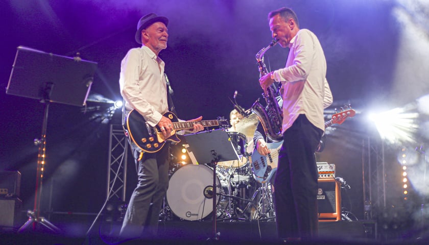 Scena oblana fioletowym światłem, dwaj mężczyźni grają na gitarach. Koncert VooVoo w Centrum Historii Zajezdnia 24.08.2024