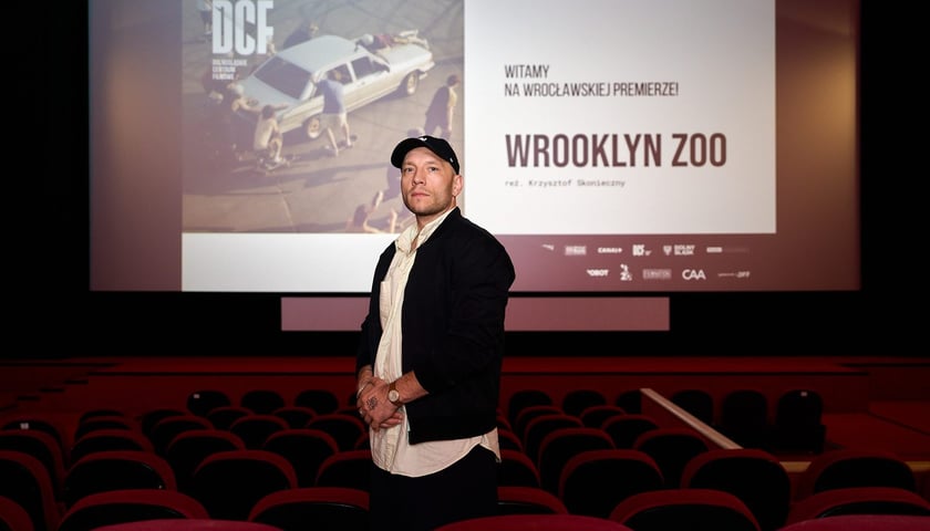 Na zdjęciu Krzysztof Skonieczny w sali kina DCF na tle ekranu, na którym wyświetlona jest zapowiedź filmu „Wrooklyn Zoo”