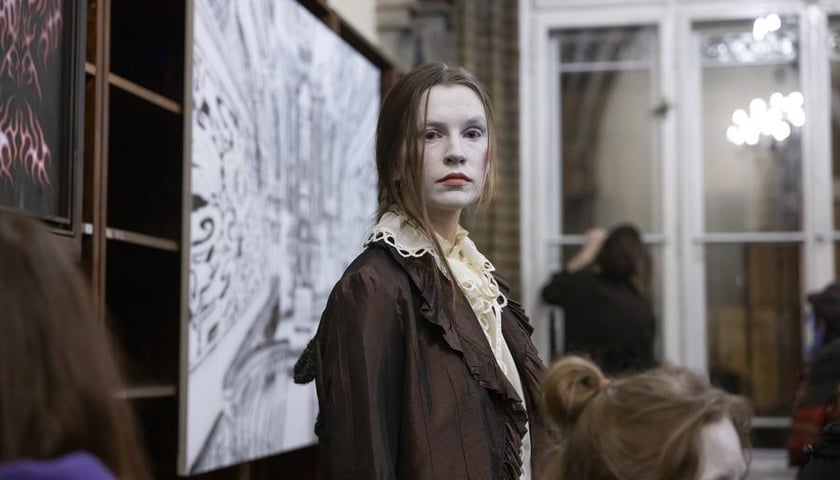 Performerka Agnieszka Raczkowiak z twarzą pomalowaną na jasny, surowy kolor, stojąca przy pracy plastycznej na wernisażu wystawy Dark Academia Kościoła Nihilistów w bibliotece na Szajnochy (19 października 2024)