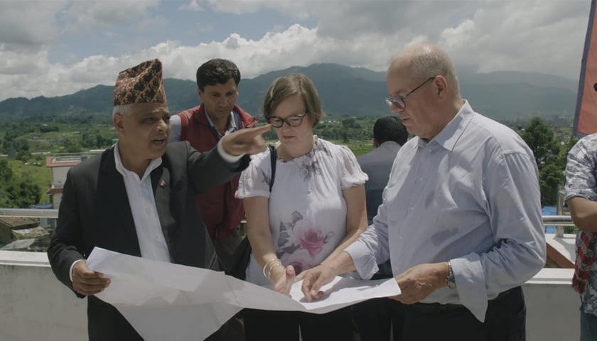 Kadr z filmu "Plan na raj". Na zdjęciu cztery osoby oglądają plan architektoniczny. W tle za ich plecami górski krajobraz.