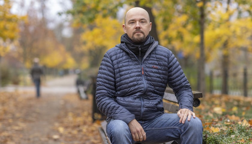 Piotr Turkiewicz (w kurtce) siedzi na ławce przy Promenadzie Staromiejskiej