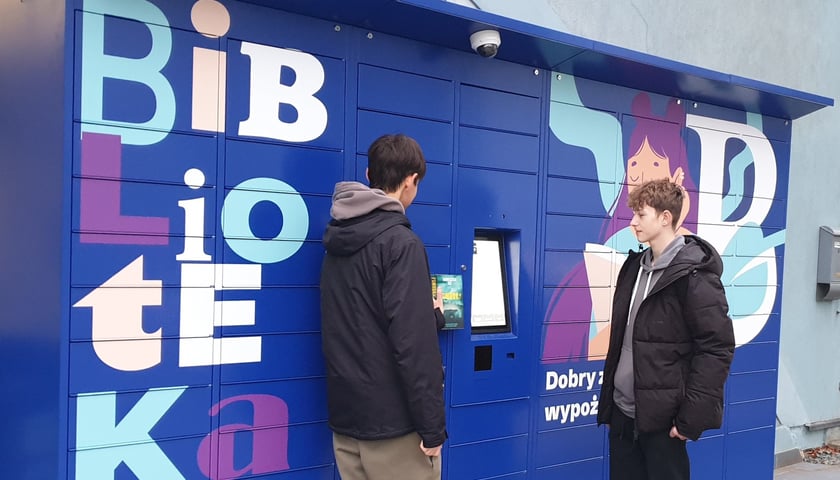 Książkomat, który od soboty będzie działał przy filii nr 22 Miejskiej Biblioteki Publicznej im. Tadeusza Różewicza przy ul. Chociebuskiej we Wrocławiu. Na zdjęciu stoją przed nim dwie młode osoby.