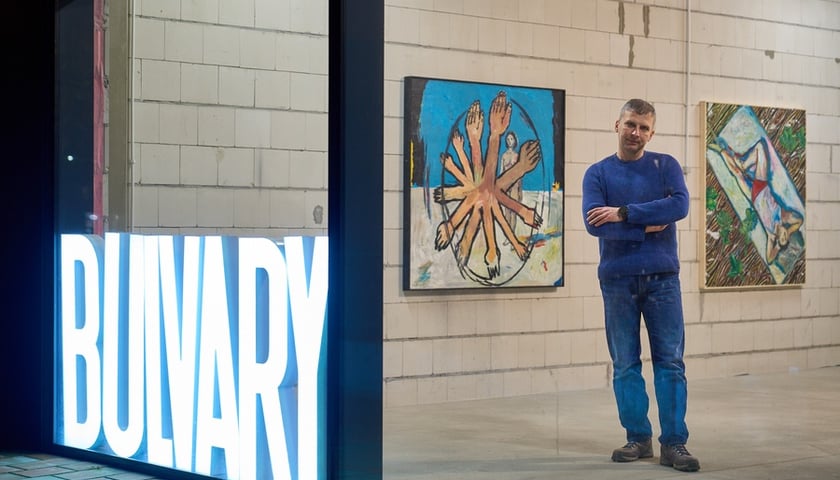 Na pierwszym planie jest neonowy napis Bulvary, na drugim Hubert Bujak, za nim dwa jego obrazy wiszące na ścianie