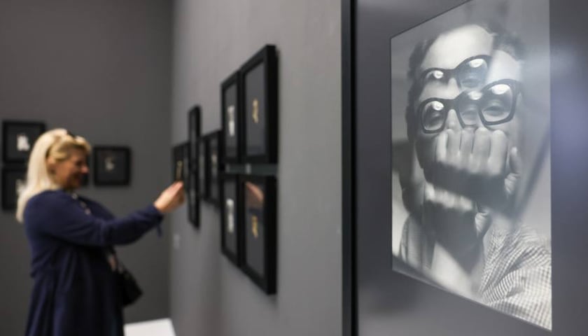 Fotograficzny autoportret Zdzisława Beksińskiego na ścianie Pawilonu Czterech Kopuł, w tle kobieta oglądająca wystawę (13 kwietnia 2025)